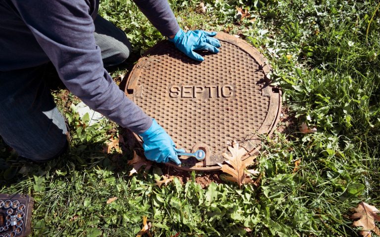 septic truck technician removing septic tank cover 768x480